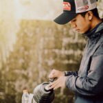 Indonesian man pouring coffee from pot into cups outdoors at a street stall.