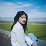 Portrait of a woman in Indonesia posing by a vibrant green rice field under a blue sky.