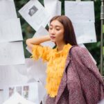 Fashionable woman in vibrant attire posing among papers, creating an artistic aesthetic.