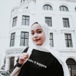 Portrait of a young woman in hijab smiling by a historical building in Indonesia.