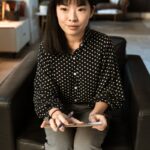 Asian woman sitting in an office setting, preparing for a job interview with a tablet in hand.